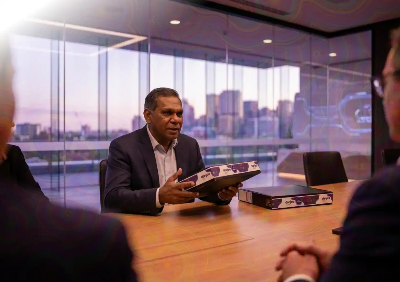 A business meeting in a modern conference room, a professional holding a Danjoo branded box.