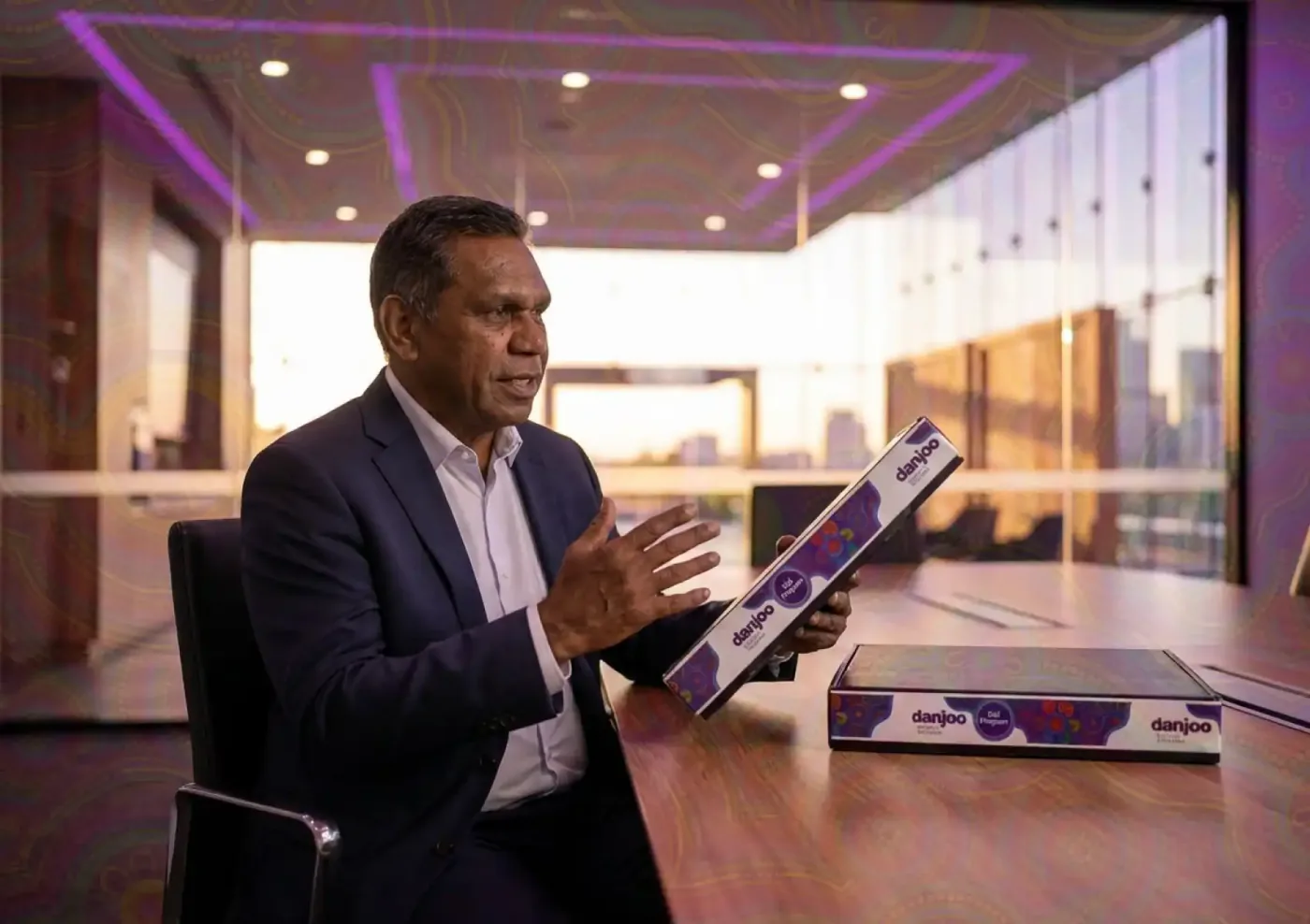 A Danjoo representative presenting a branded box with circular Aboriginal artwork during an office meeting.