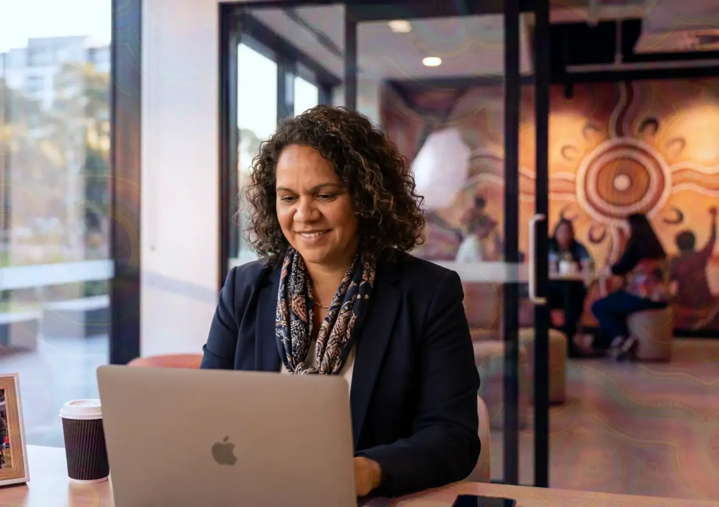 A professional working on a laptop in a modern office with a mural backdrop.