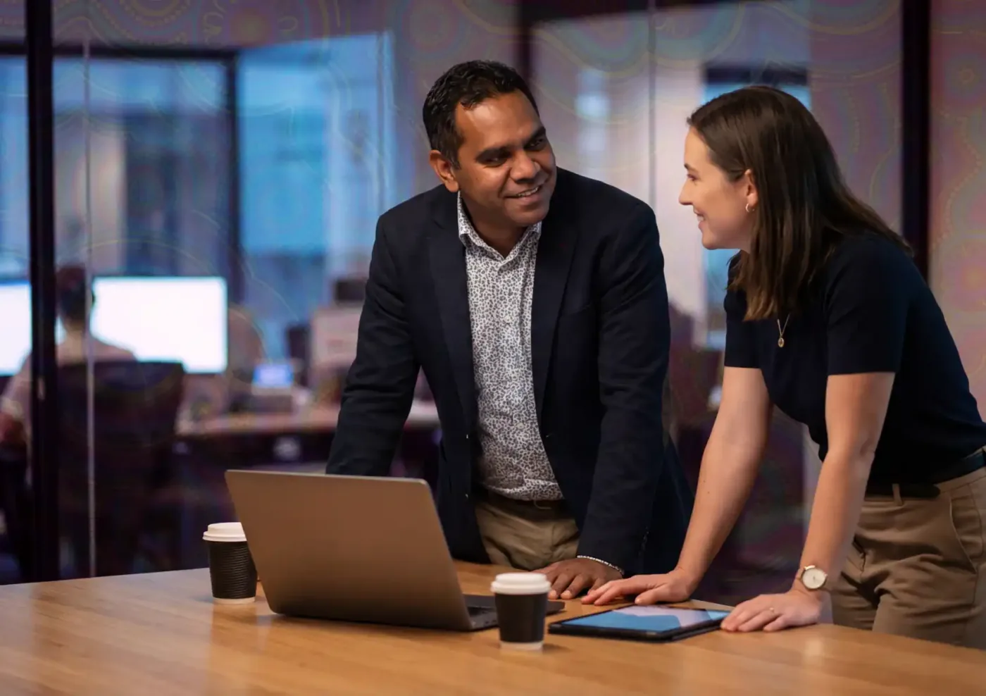 Two professionals collaborating at an office table with a laptop and tablet.
